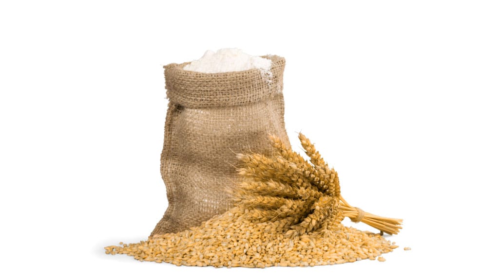 a bag of flour with a pile of unground wheat grains in front of it on white background