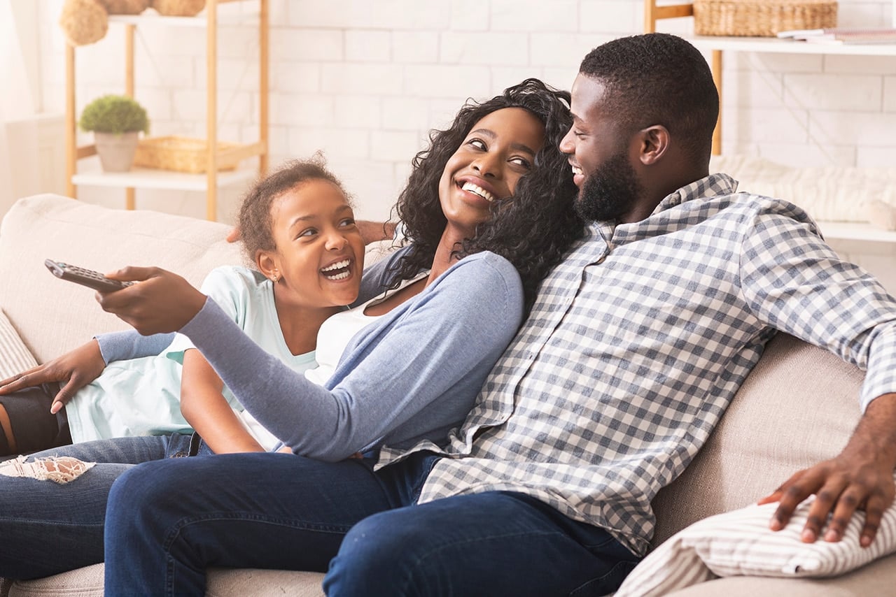 smiling family sitting on a couch watching tv together