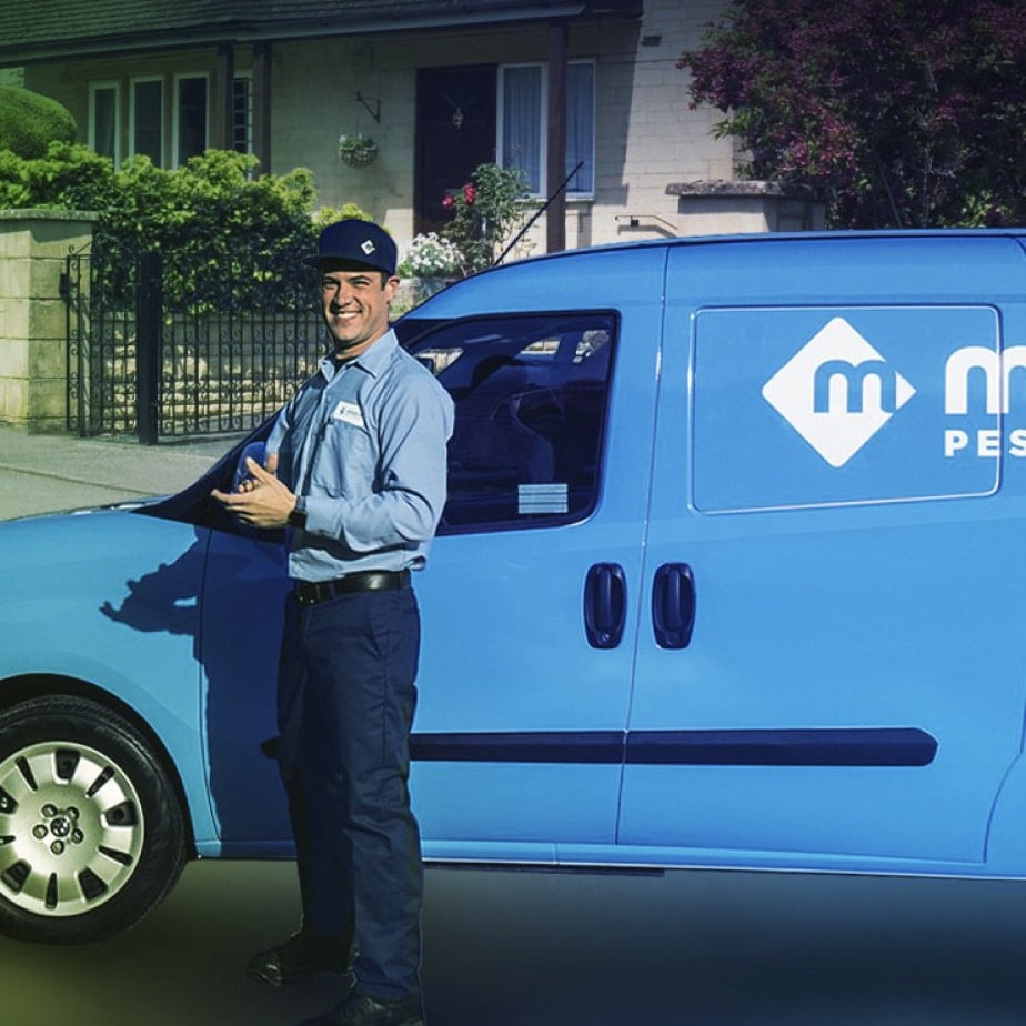 moxie pest control services technician standing in front of his van in a neighborhood