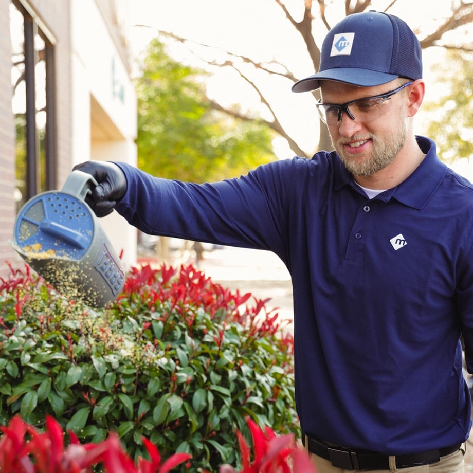 Moxie Pest Control Technician applying granules for pests in flower bed
